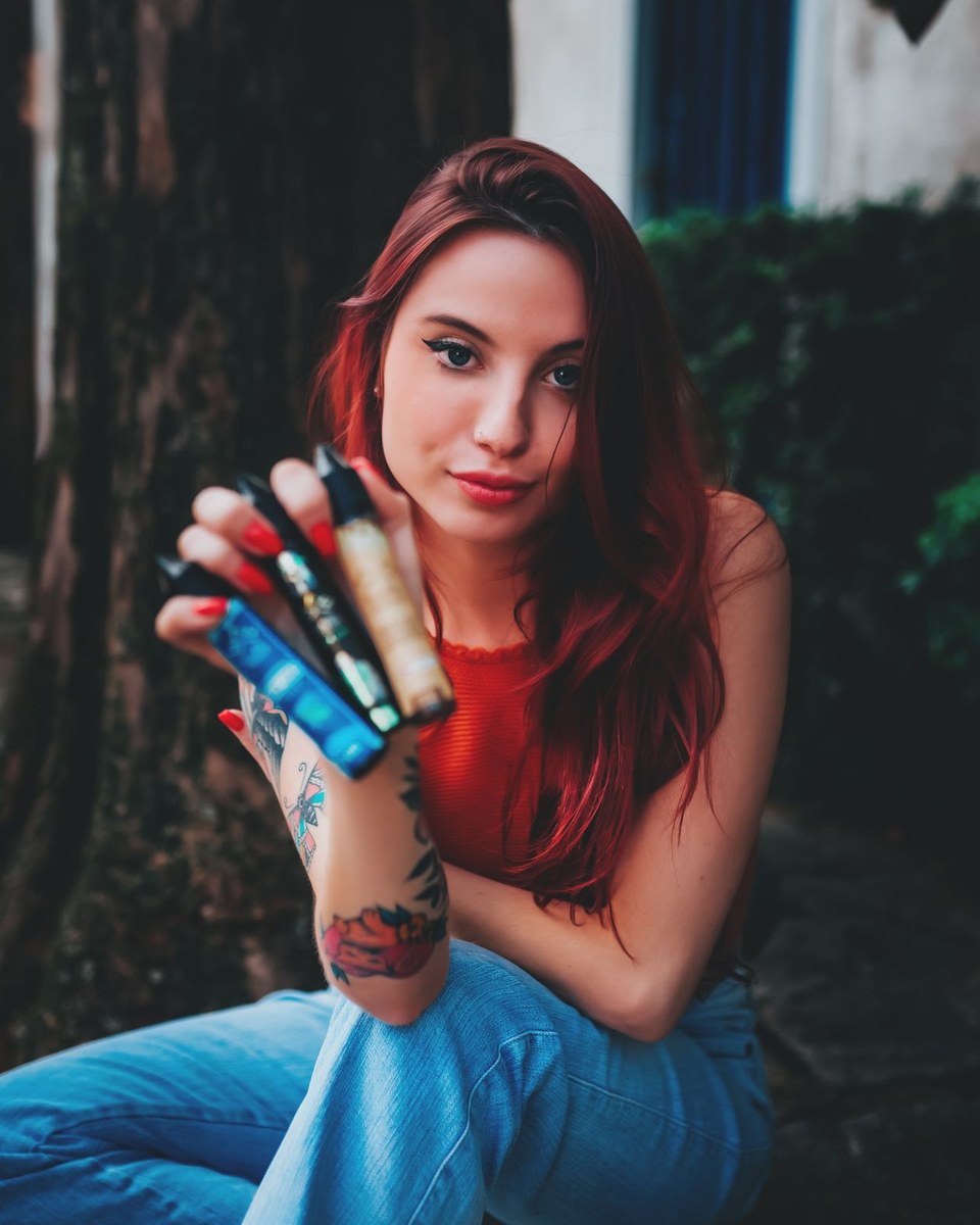 Adult holding multiple refillable vape pens and e-liquid bottles toward the camera in outdoor daylight