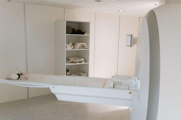 Patient table extending from a large white medical imaging scanner in a bright hospital room, with positioning pads on a shelf